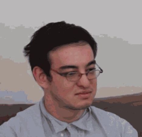 a man wearing glasses sitting in front of a computer monitor with his head turned to the side