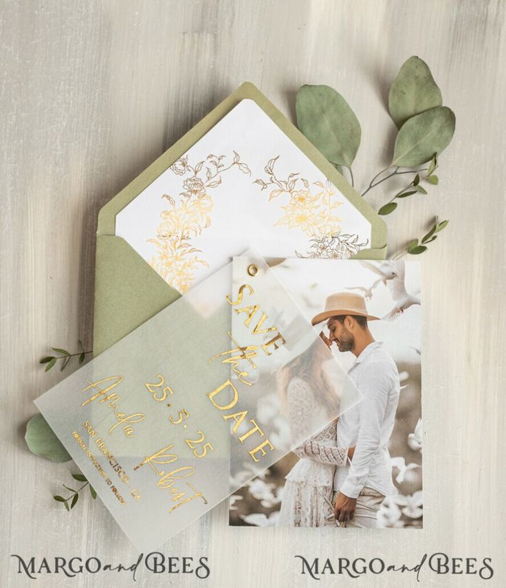 the wedding stationery is laid out on top of each other, with greenery and gold foil