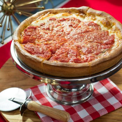 a deep dish pizza sitting on top of a metal platter next to a red checkered tablecloth