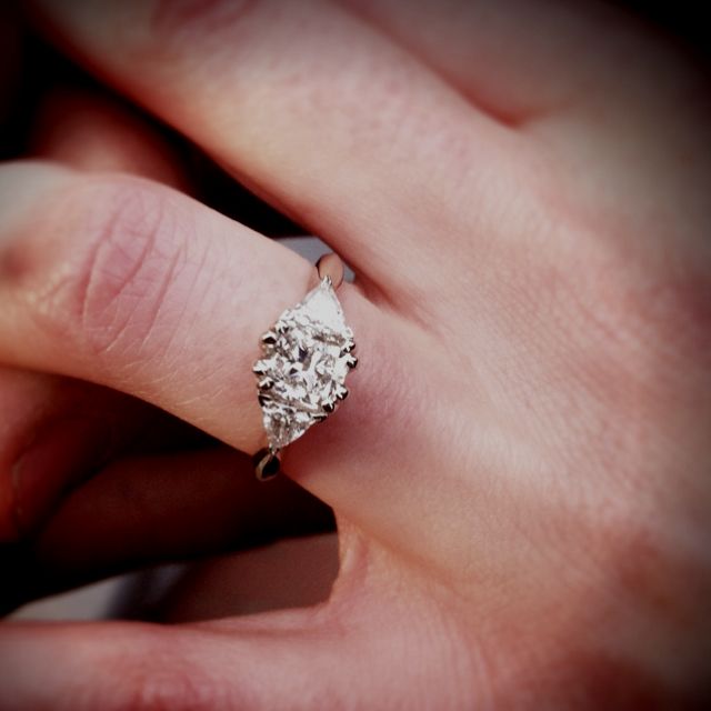 a woman's hand holding an engagement ring with a diamond in the middle, on top of her finger