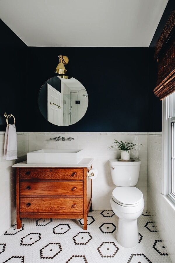 a white toilet sitting next to a wooden dresser in a bathroom under a round mirror