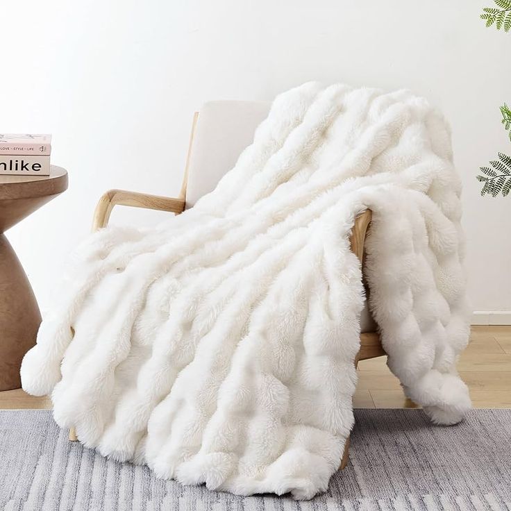 a white fluffy blanket sitting on top of a wooden chair next to a potted plant