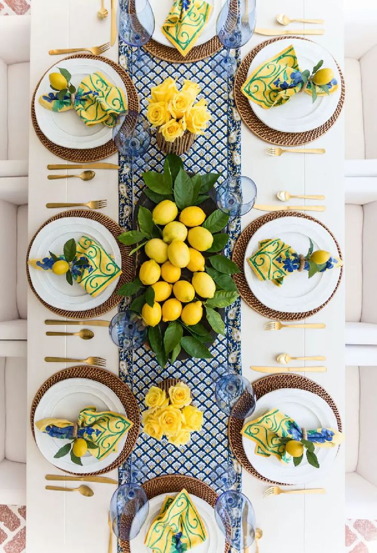 the table is set with yellow flowers and lemons on it, along with white plates