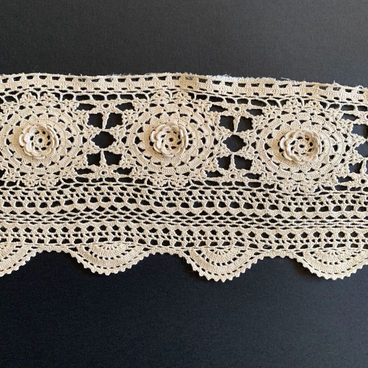 a piece of crocheted lace with flowers on it's edge, sitting on a black surface