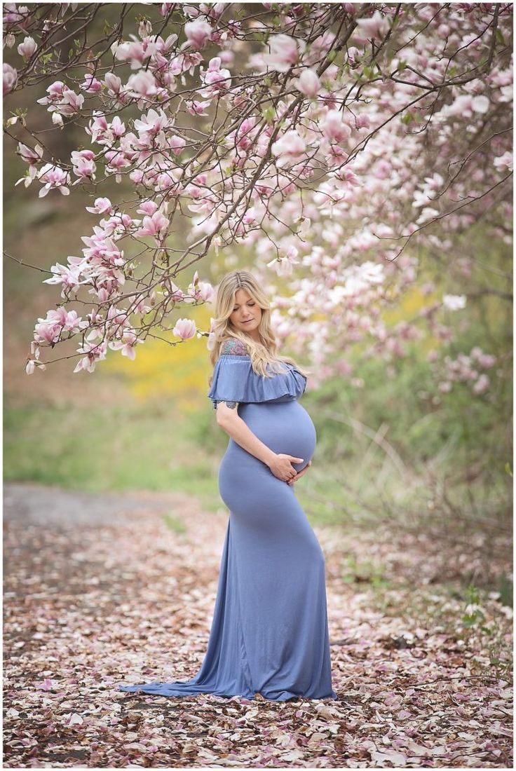 a pregnant woman in a blue dress standing under a tree with pink flowers on it