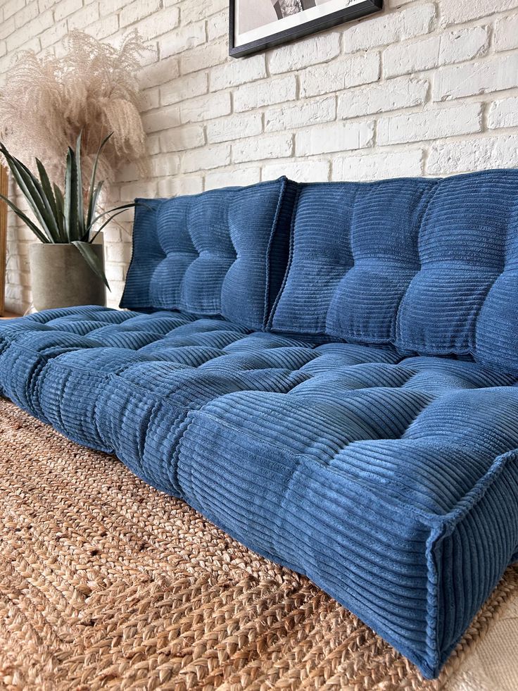 a blue couch sitting on top of a wooden floor next to a plant in a vase