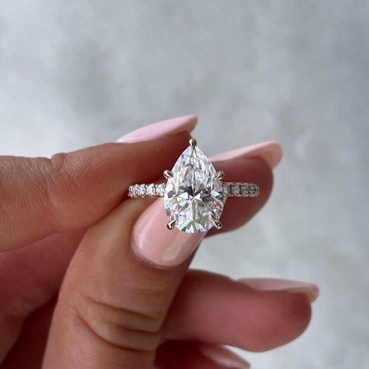 a woman's hand holding an engagement ring with a pear shaped diamond on it