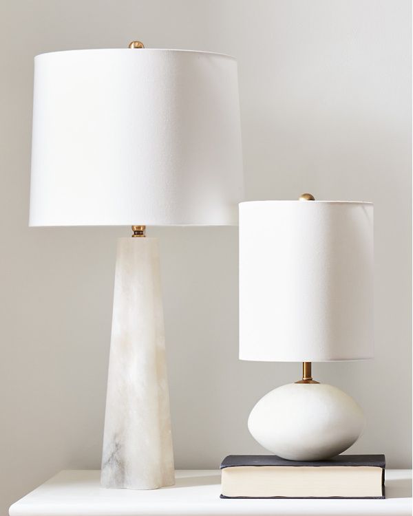 two lamps sitting on top of a white dresser next to a book and lamp shade