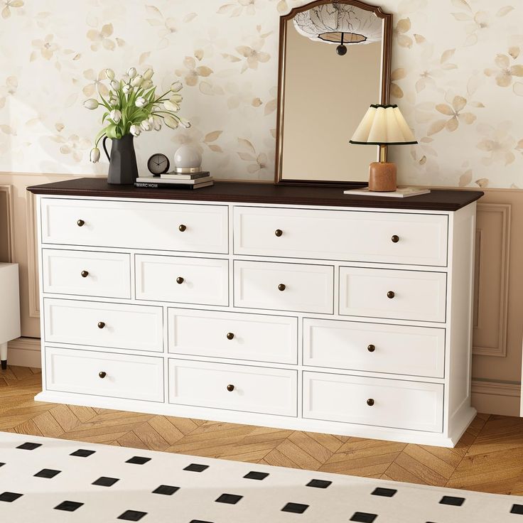 a white dresser sitting next to a lamp and a mirror on top of a wooden floor