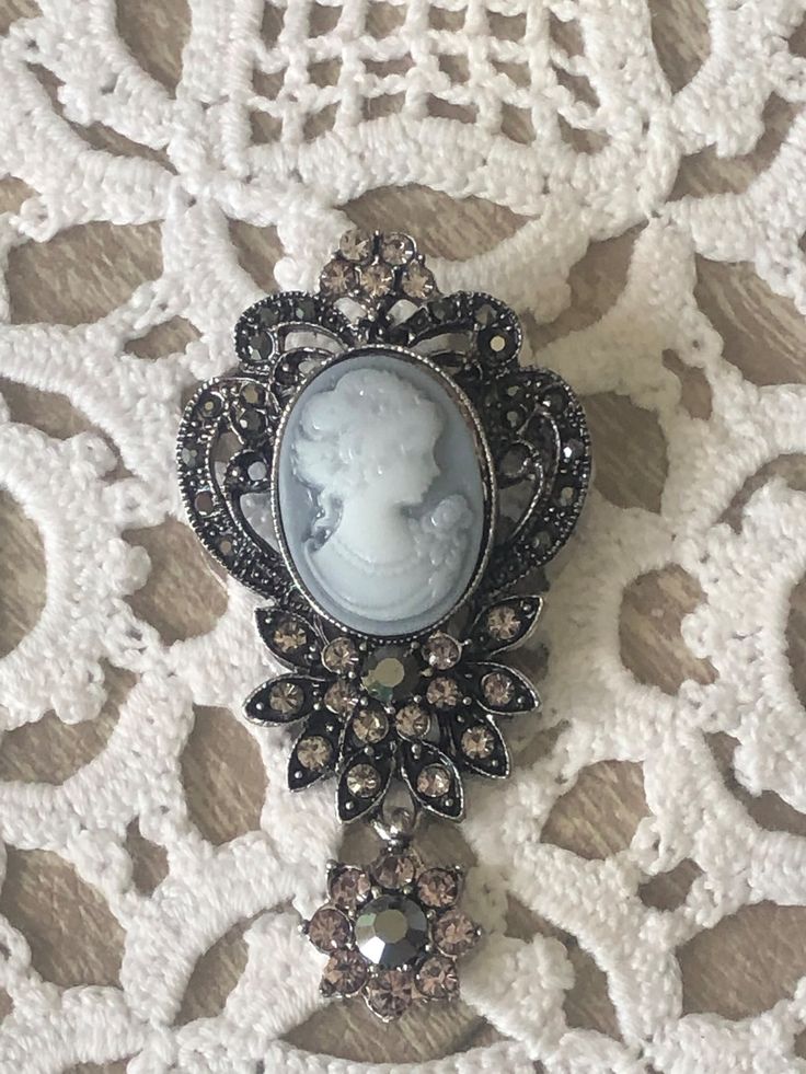 A two tone Gray Cameo is lovely in this marcasite-like setting with crystals and a crystal drop. This is a faux cameo brooch but it looks very vintage on a blouse, dress, coat, and sweater. You will surely receive many compliments. This cameo will be sent in a gift box.  If you want this complementary wrapped, please make a note of such in the comments section. All shipments are combined to save on postage costs.  Please email seller if you have any questions. We use USPS First Class Mail and if you need Signature Confirmation pls make a note in the Comments section and add USPS fee of $3.45. Thank you for looking at this Etsy.com shop. Silver Victorian Pins, Groom Lapel Pin, Farmhouse Floral Decor, Hot Air Balloon Centerpieces, Long Beach Ny, Fall Mason Jars, Silver Brooch Pin, Starfish Pendant, Elegant Lady