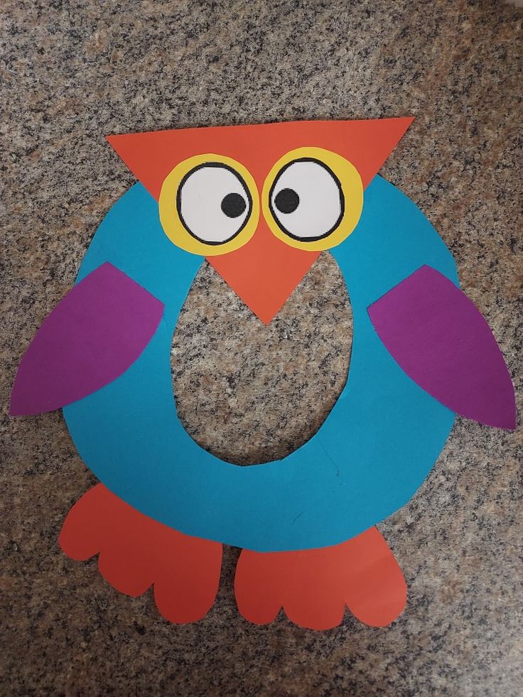 an owl cut out from cardboard sitting on top of a granite floor next to a paper circle