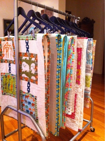 an ironing board with several different quilts hanging from it's sides on a wooden floor