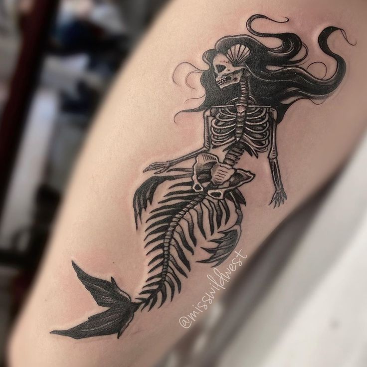 a woman's arm with a skeleton and fish tattoo on the left side of her body