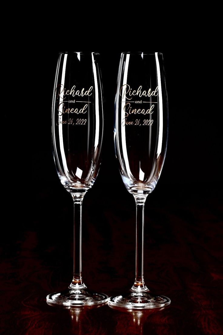 two wine glasses sitting next to each other on top of a wooden table in front of a black background