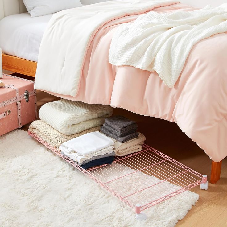 a bed with pink and white sheets on it, next to a small chest of drawers