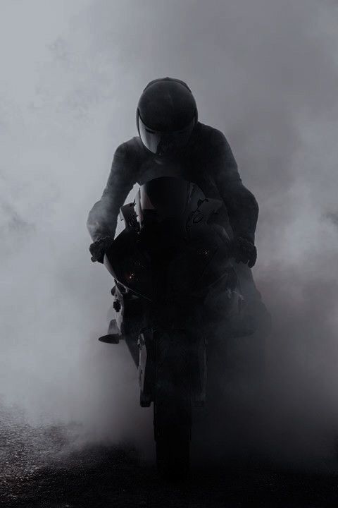 a man riding on the back of a motorcycle down a foggy road at night