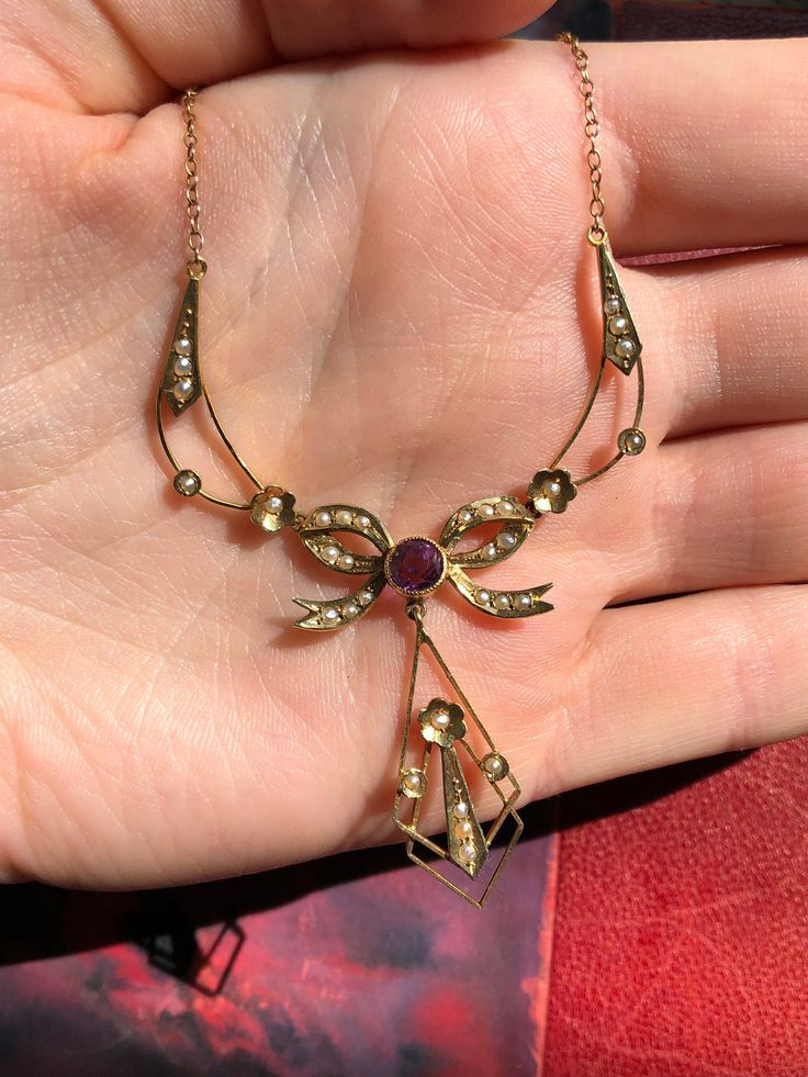 Stunning Edwardian 14k necklace. Stamped 14k but it tests 14k in some parts and 10k in others. In amazing condition. Very romantic and sweet with seed pearls and a bow. The purple stone is likely amethyst but it has not been tested. Will be sent with tracking and in a gift box.  14.5" long (meant for a size small neck) The pendant section is 3" long The hanging piece off the bow is 1" long 4.15 grams in weight Antique Yellow Gold Jeweled Necklaces, Antique Yellow Gold Necklaces With Jewels, Formal Fine Jewelry Amethyst Necklaces, Formal Fine Jewelry Amethyst Necklace, Formal Amethyst Necklace In Fine Jewelry Style, Fine Jewelry Gemstone Necklace Collectible, Antique Pendant Diamond Necklace Gift, Antique Diamond Necklace With 17 Jewels For Anniversary, Collectible Fine Jewelry Necklaces With Gemstones