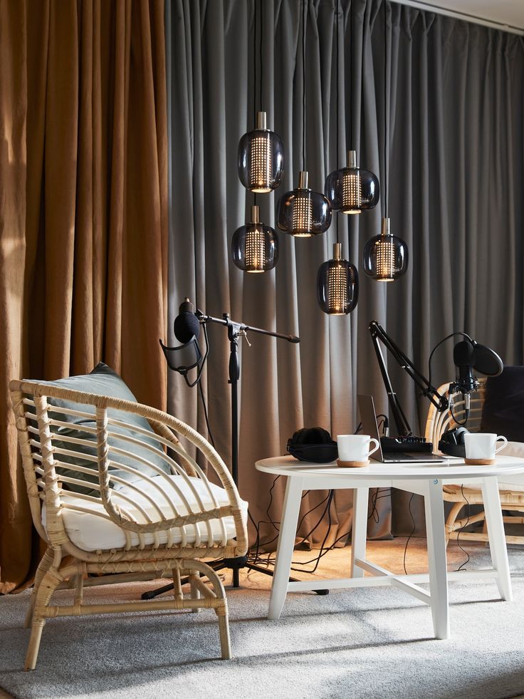 two chairs and a table in front of a curtained wall with lamps on it