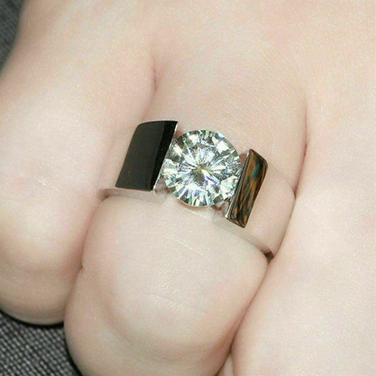 a person's hand holding a ring with a diamond on it and a black band