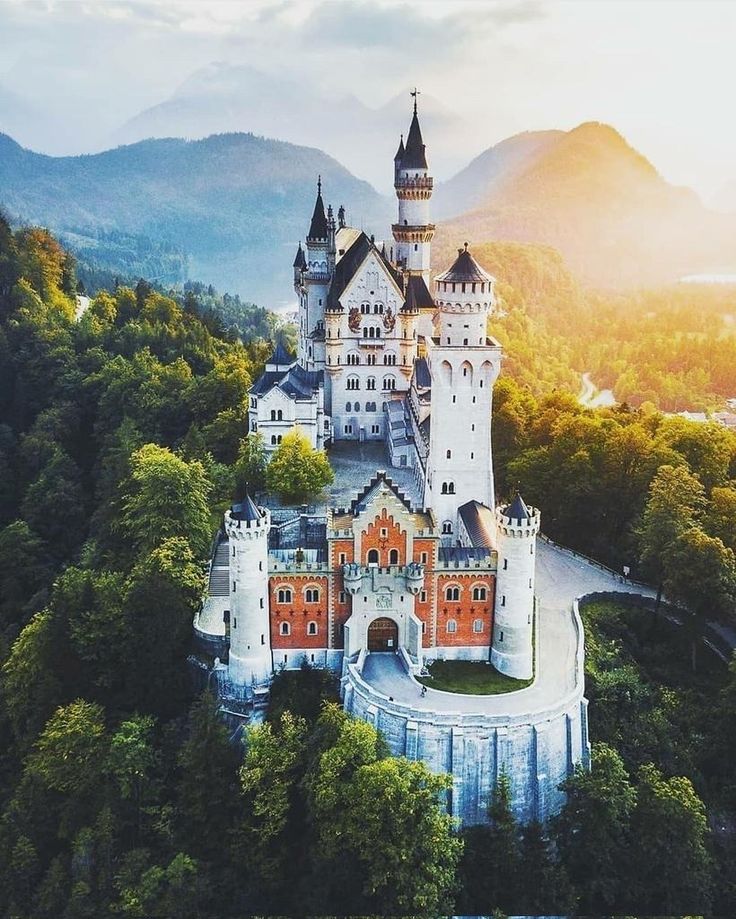 an aerial view of a castle in the middle of trees and mountains with sunlight shining on it