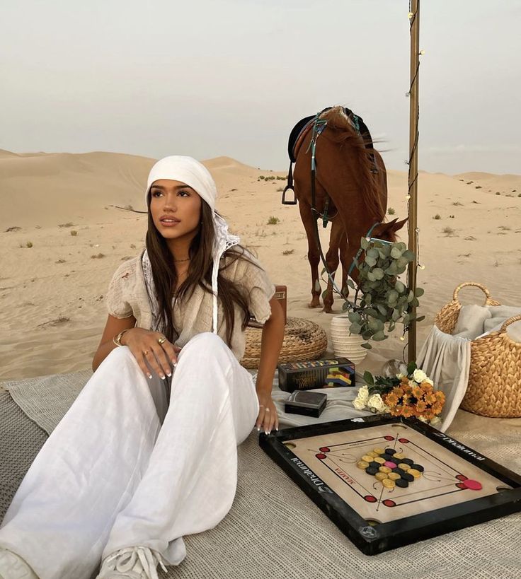 a woman sitting on the ground next to a table with food and a horse in the background