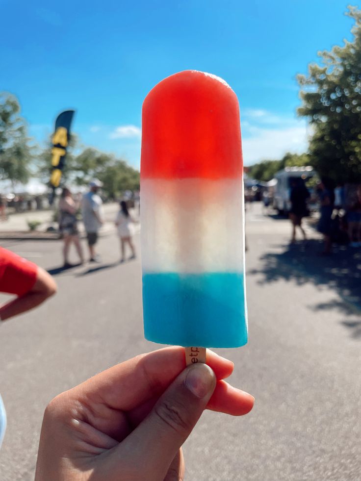 a hand holding an ice cream popsicle with red, white and blue icing