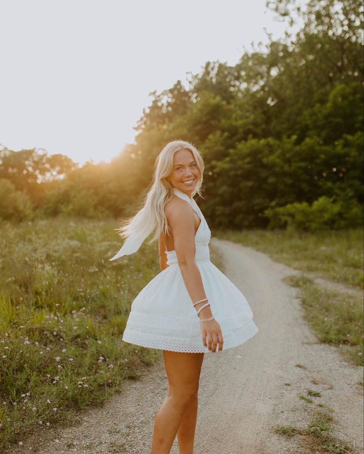 a woman in a white dress standing on a dirt road