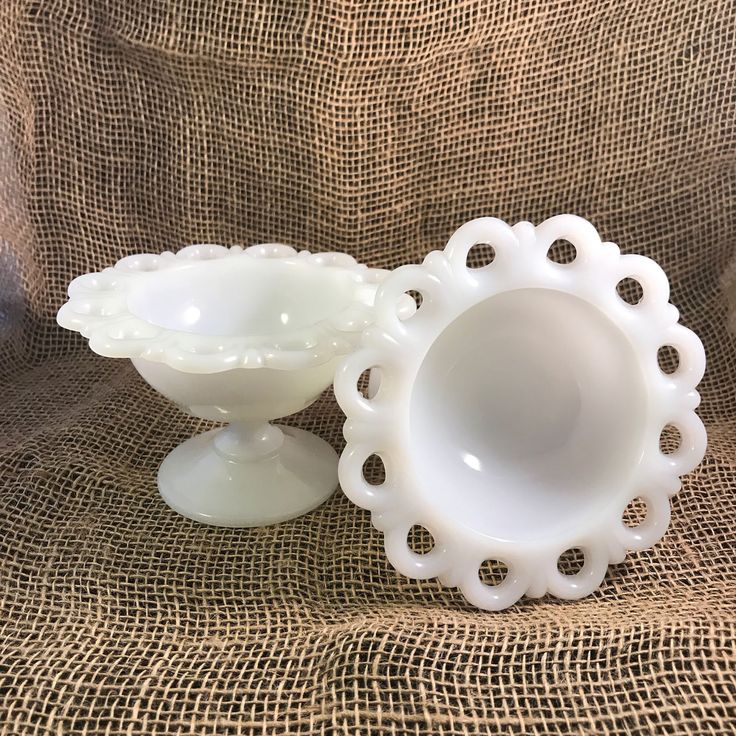 two white vases sitting on top of a brown cloth