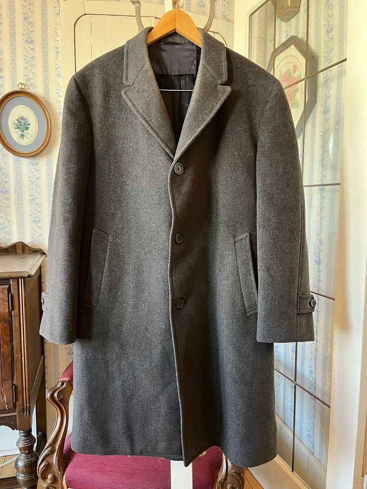 This simple overcoat from Panda by Whitehall is made from a wool blend in charcoal grey. It has the original buttons, two front pockets and two inside pockets, and it's fully lined with black silky lining. The measurements, taken with the coat lying flat, are: shoulder to shoulder,  18 inches; armpit to armpit, 22 inches; sleeves, 25 inches; length, 42 inches; bottom edge, 32 inches. Please note that there is some discolouration around the collar and a repair has been made in the back - see phot Gray Single-breasted Wool Coat, Gray Wool Coat With Button Closure, Classic Gray Wool Coat For Winter, Classic Gray Wool Coat For Fall, Gray Wool Coat With Pockets, Gray Single Breasted Long Wool Coat, Gray Single-breasted Long Wool Coat, Classic Gray Wool Coat With Pockets, Gray Business Wool Coat With Pockets