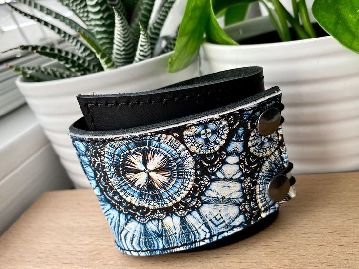 "I've made this wrapping cuff out of smooth leather with a digital print design. Choose from a brown or black leather base. It has attached elastics that hook over two rivets so this cuff will adjust to fit most wrist sizes 6 to 7.5\" in circumference. The cuff is 2\" wide at the narrowest and 2.75\" at the widest end. This cuff is quite unique, I get lots of feedback comments such as: \"I have hard to fit wrists and it fits perfectly.\" \"The leather is so soft and feels great on my skin.\" \"B Handmade Blue Leather Bracelet For Festival, Handmade Blue Leather Festival Bracelet, Adjustable Blue Cuff Bracelet For Festivals, Blue Cuff Bracelets For Festivals, Adjustable Cuff Bracelet With Wrist Strap, Blue Cuff Bracelet Gift, Blue Cuff Bracelet For Festival, Adjustable Blue Bracelets In Wearable Art Style, Blue Adjustable Unique Cuff Bracelet