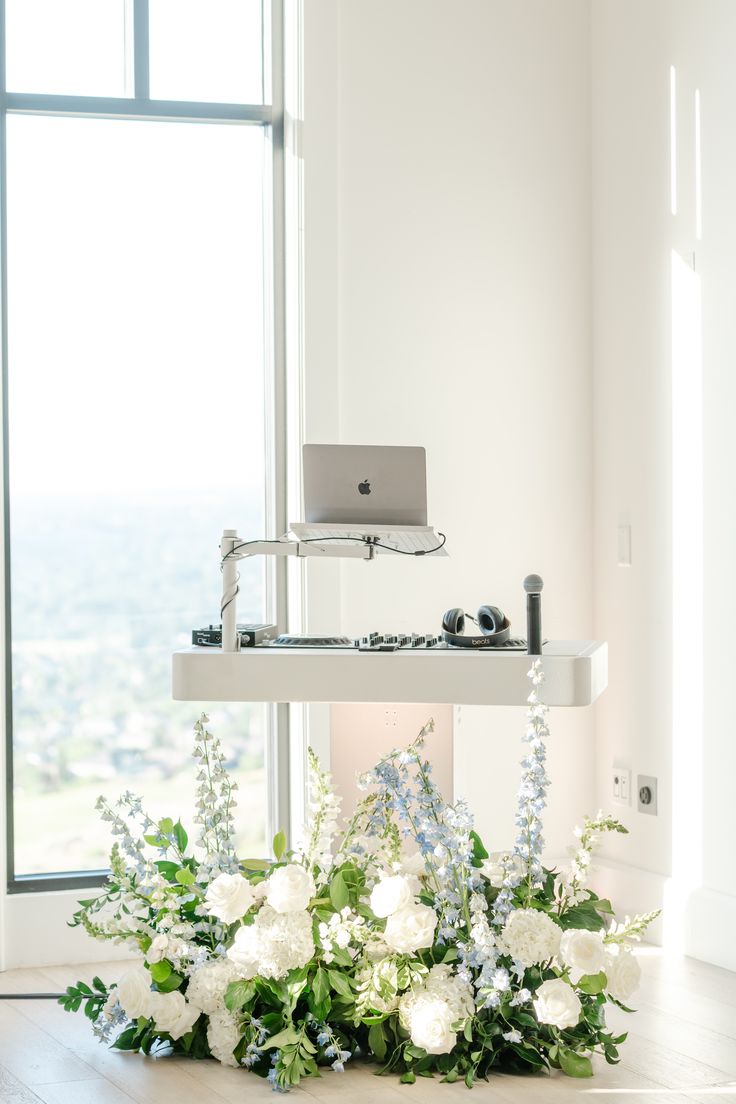 a laptop computer sitting on top of a table with flowers in front of the window