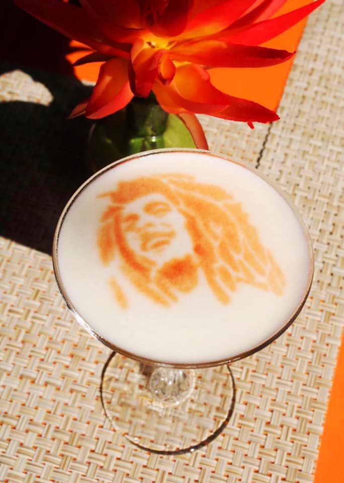 an orange flower sitting on top of a table next to a glass filled with liquid