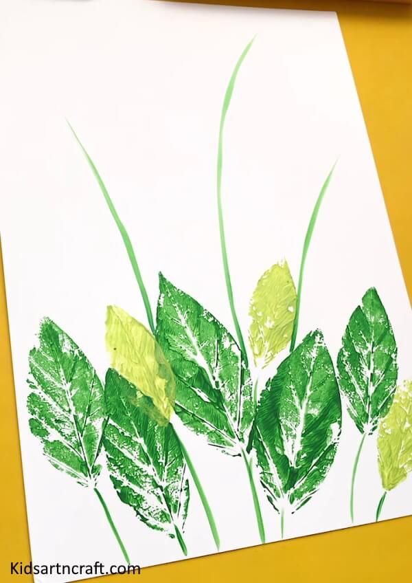 an art project with green leaves on white paper and watercolor pencils in the background