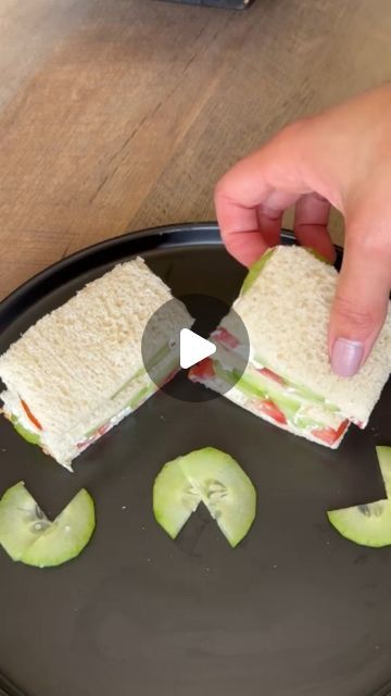 someone cutting into a sandwich on top of a black plate with slices of apple next to it