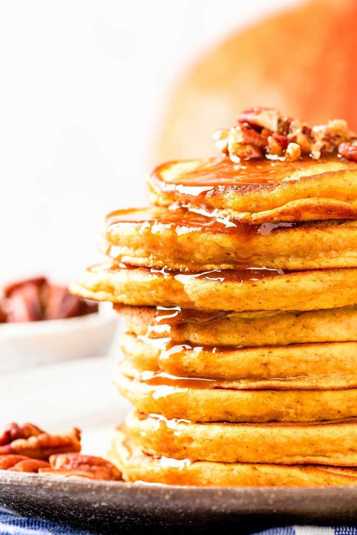 stack of coconut flour pumpkin pancakes on a plate with maple syrup and pecans in the background