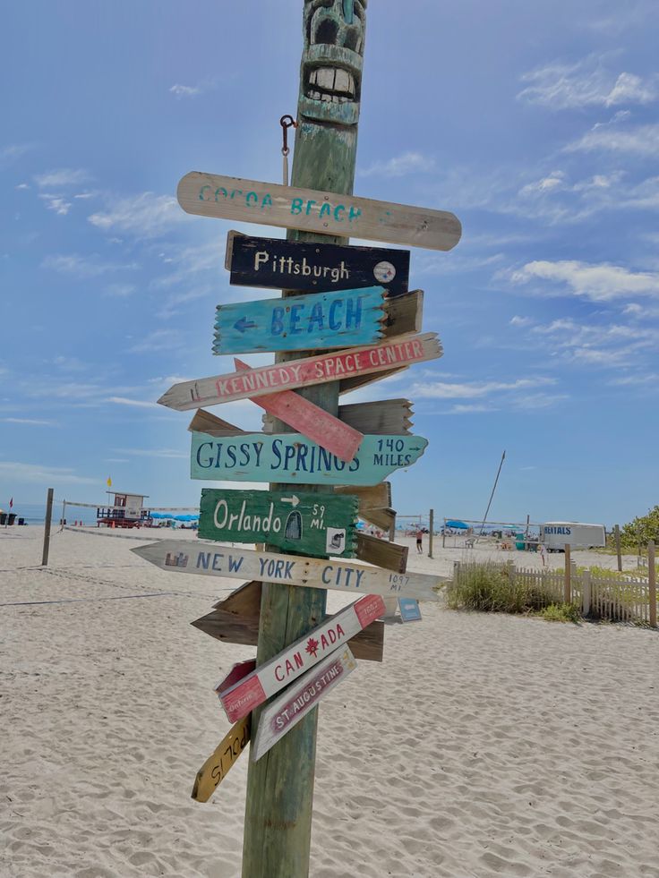 a wooden pole with many different signs on it at the beach in front of some sand