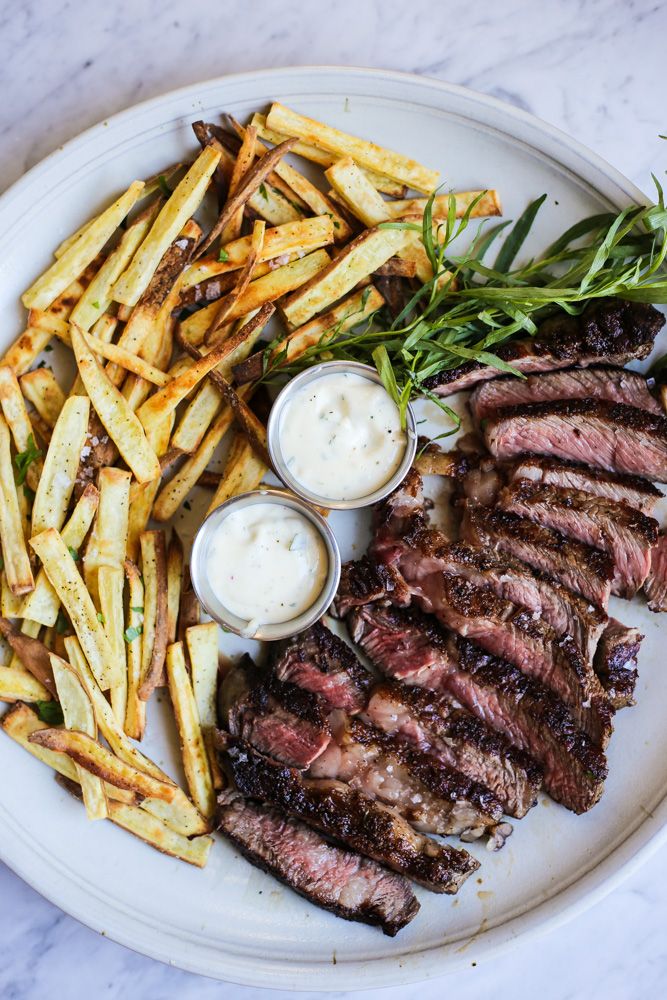 steak and french fries on a white plate with ranch dressing in small bowls next to them