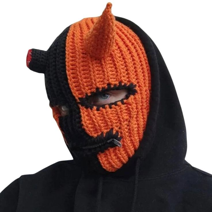 a man wearing an orange and black knitted mask with horns on it's face