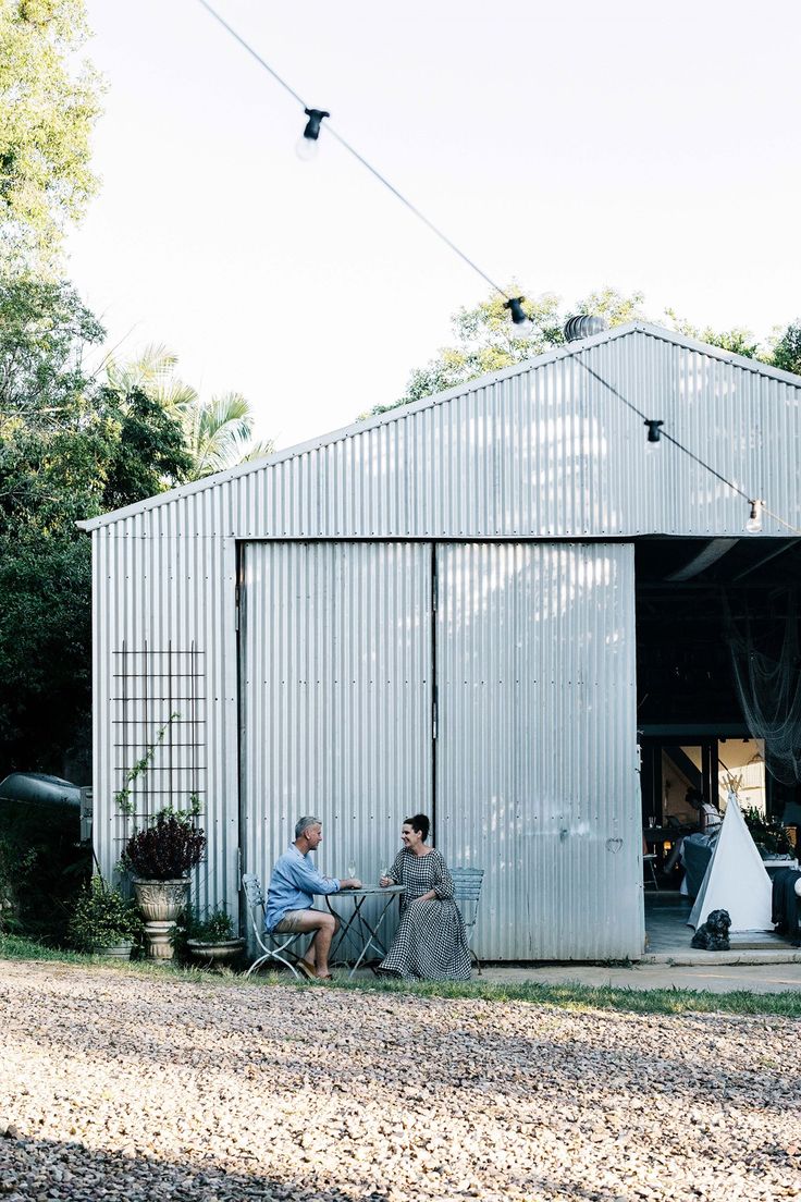 two people sitting in lawn chairs outside of a white building with an awning over it