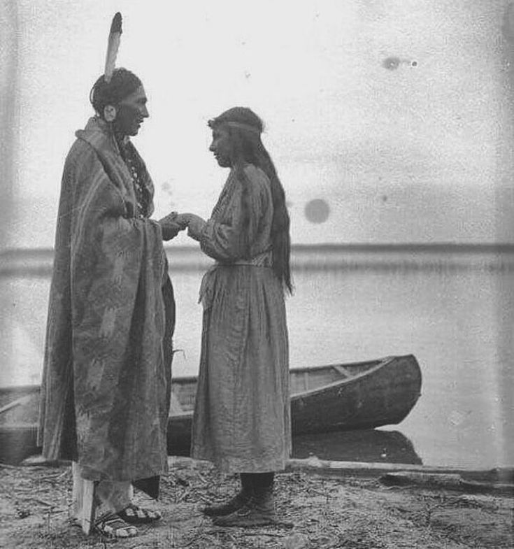 two native americans standing next to each other in front of a boat on the water