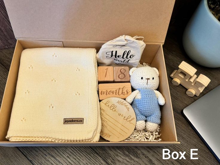 an open box containing a baby's blanket, teddy bear and other items next to a laptop