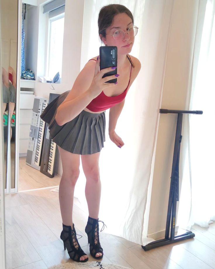 a woman taking a selfie in front of a mirror with her cell phone while standing on the floor