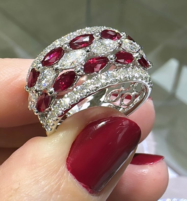 a woman's hand holding a red and white ring with diamonds on top of it