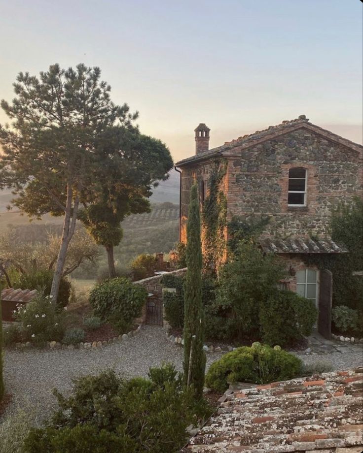 an old stone house surrounded by greenery in the countryside at sunset, with trees and bushes surrounding it