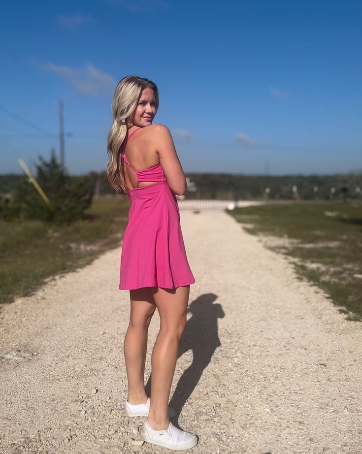 Blonde haired white woman standing on a dirt road wearing a bright pink womens activewear dress. Summer Athleisure Dresses With Built-in Bra, Sporty Spring Dresses With Built-in Bra, Sporty Mini Dress With Built-in Bra For Workout, Mini Tennis Dress With Built-in Bra For Workout, Workout Dress With Built-in Stretch Shorts, Stretch Mini Dress With Built-in Shorts, Workout Dresses With Built-in Bra And Racerback, Workout Mini Dress With Built-in Bra, Summer Sporty Pink Tennis Dress