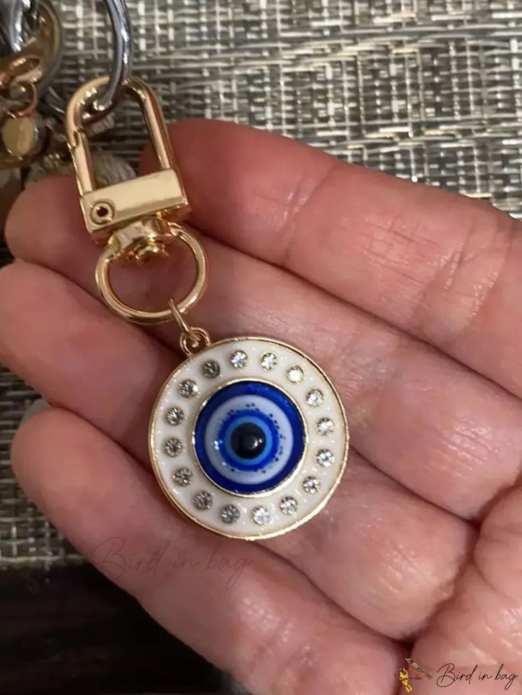 a hand holding a key chain with an evil eye on it