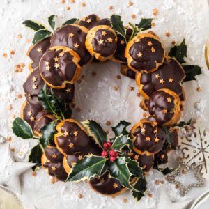 a christmas wreath made out of chocolates and holly leaves on a white tablecloth