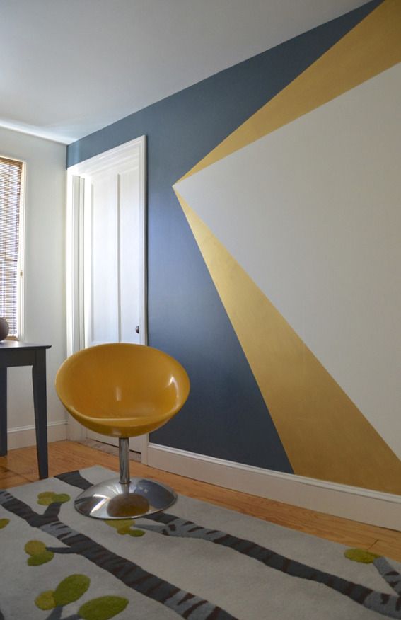 a yellow chair sitting on top of a wooden floor next to a wall painted in blue and gold