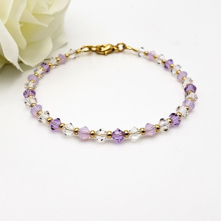 The elegant bracelet features high-quality Czech Crystals and a tasteful design with delicate lavender hues. It showcases 4mm faceted bicone-shaped crystal beads in three distinct colors - clear, lavender, and lavender opal - with gold-colored seed beads in between. You have the option to choose between a 10K gold-plated or 14K gold-filled fully closing lobster-type clasp and jump ring. Wire guards are present on each end of the bracelet to ensure durability. They serve two purposes: 1) inhibiting the wire from wearing down over time, and 2) preventing it from scratching your skin or catching on clothing. This added feature ensures that the bracelet is not only stylish but also comfortable to wear. 📏  See listing photos for sizing help. Enjoy free tracked shipping and a fabric drawstring Violet Crystal, Lavender Opal, Bracelet For Her, Ring Wire, Diy Wire Jewelry, Crystal Beads Bracelet, Unisex Bracelets, Elegant Bracelet, Birthstone Bracelets