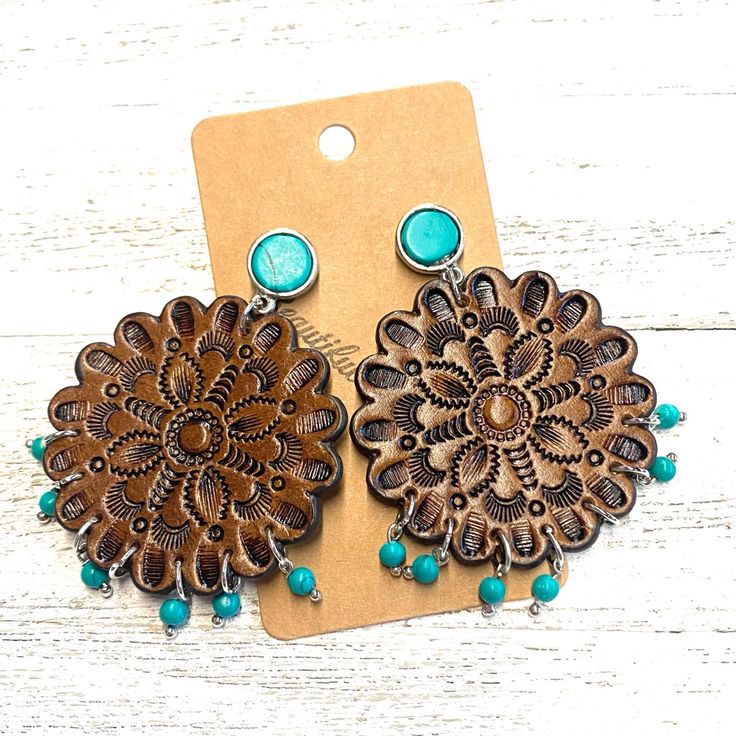 two wooden earrings with turquoise beads on top of a white wood table next to a tag